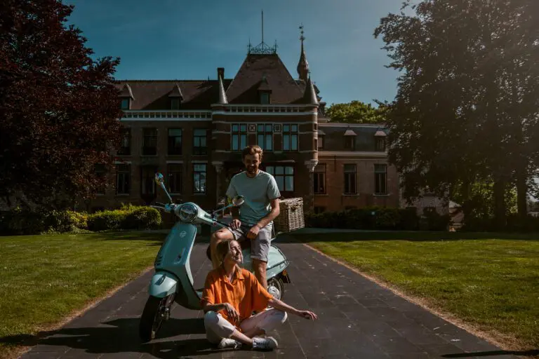twee mensen die met een Vespa voor een mooi gebouw zitten
