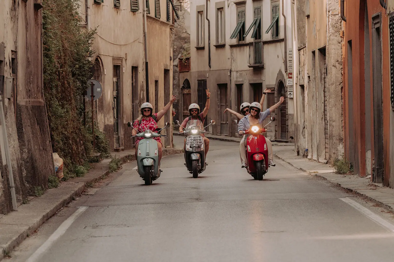 4 people on a Vespa in a small street