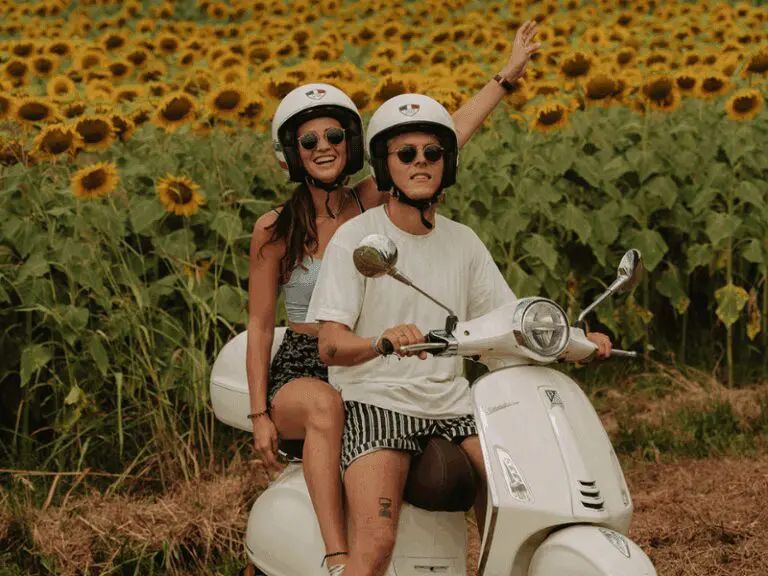 Koppel op een witte Vespa primavera met zonnebloemen op de achtergrond.