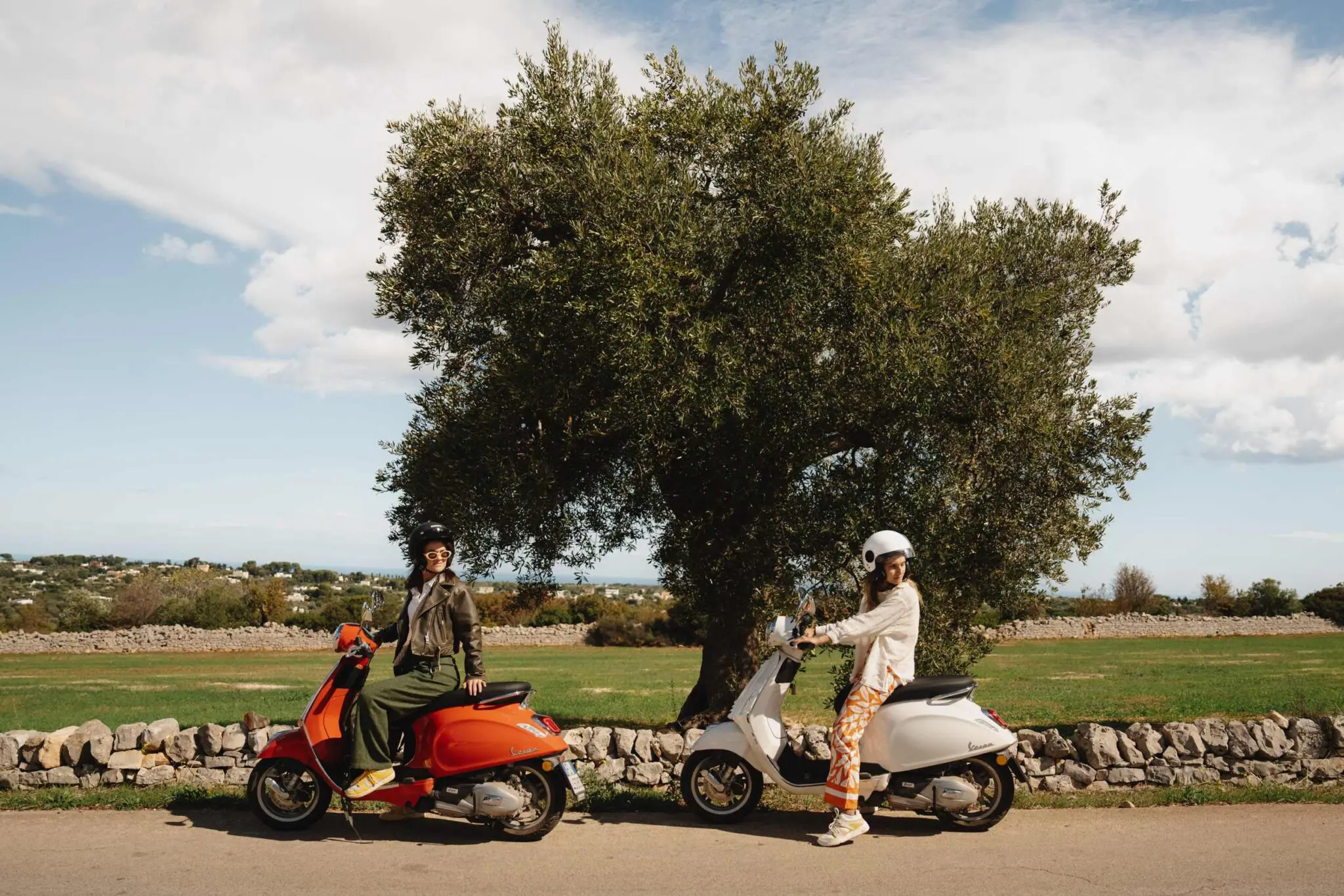 two woman on vespas infront of olive tree