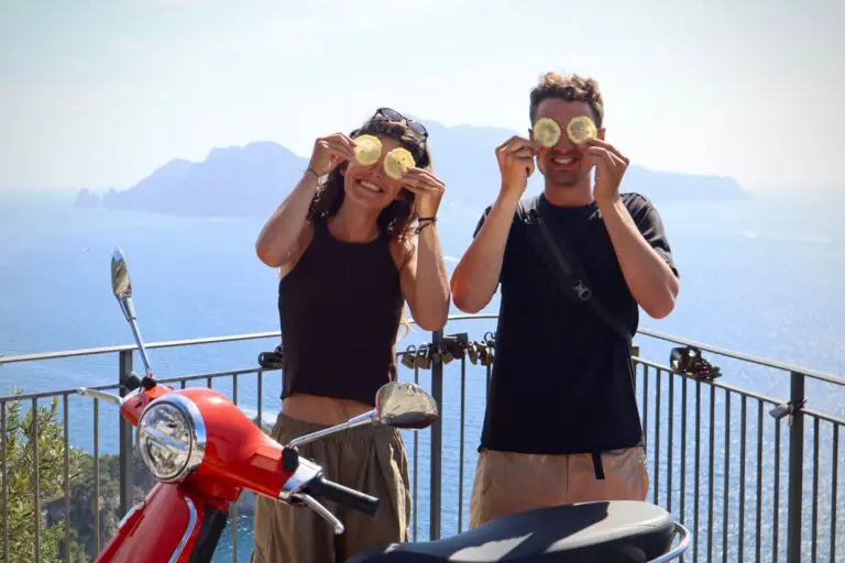 couple holding lemon slices over eyes with scooter and Amalfi Coast view