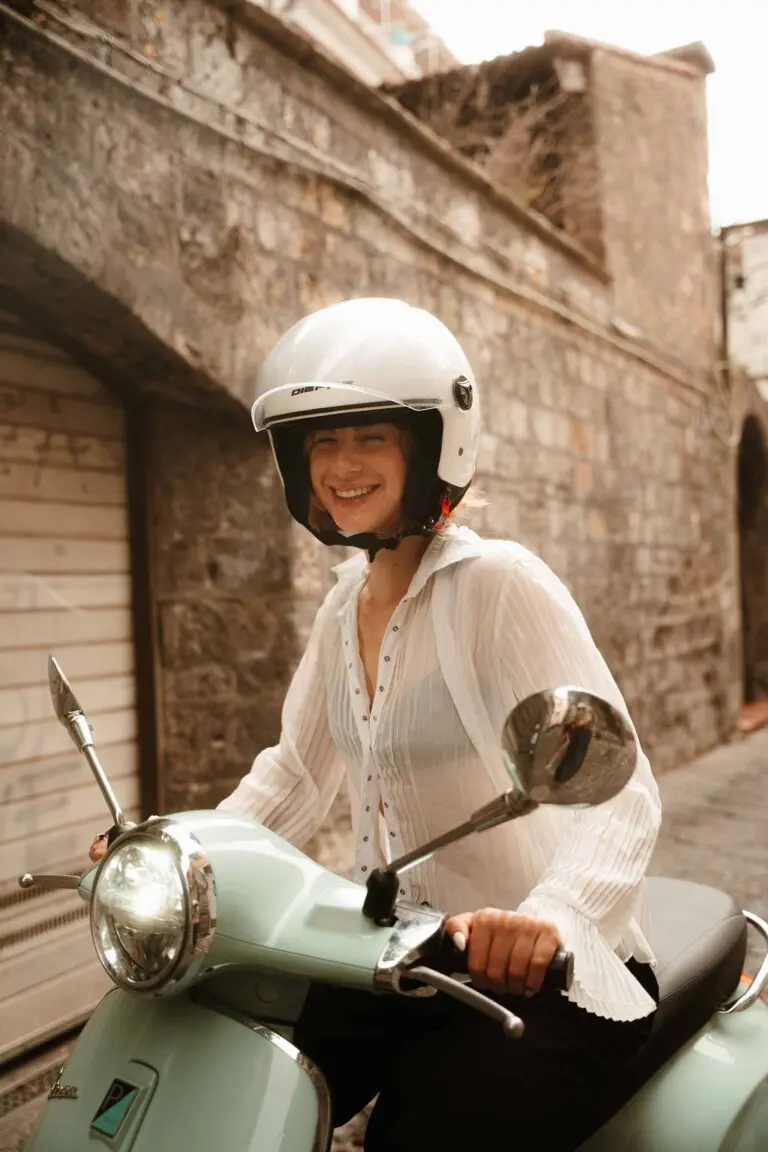 woman in helmet smiling on a mint green Vespa in Amalfi