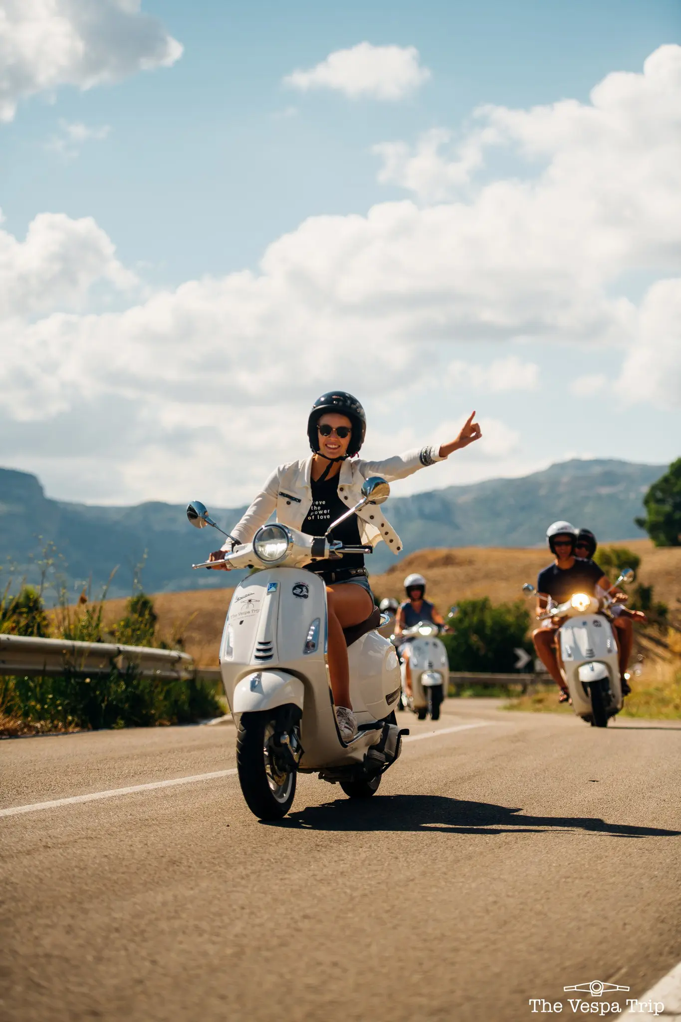 groep mensen op witte Vespa’s op een zonnige weg in Sicilië