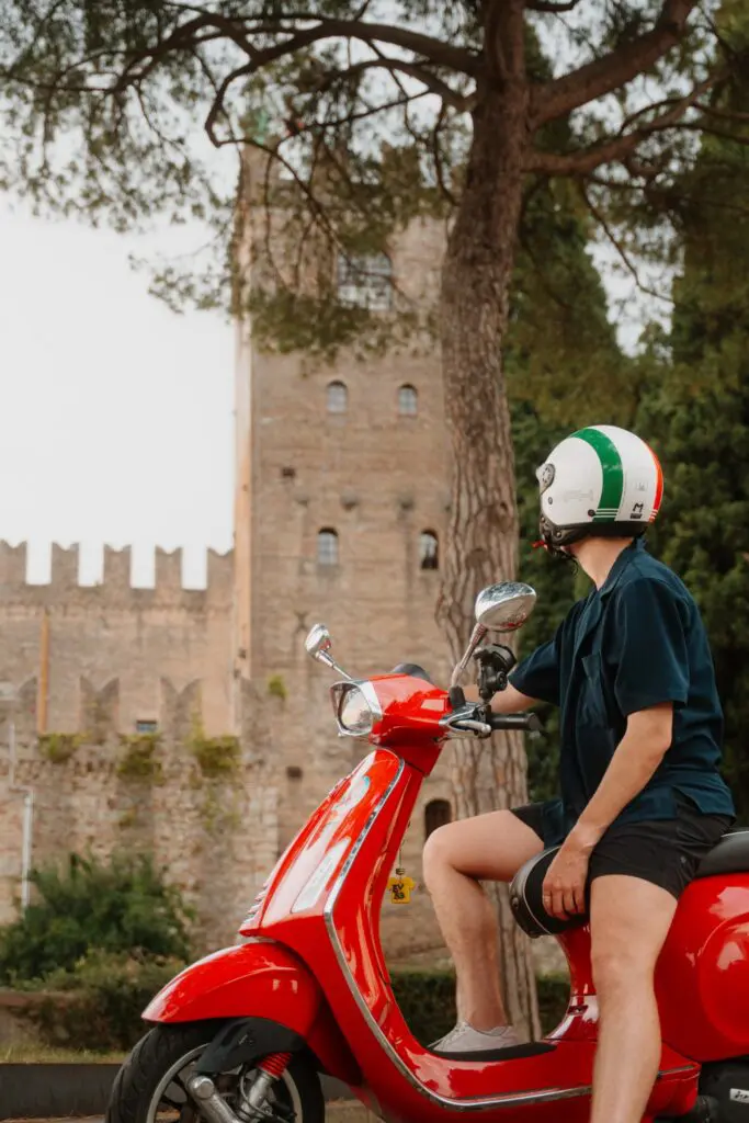 person on red Vespa scooter in front of historic Italian castle