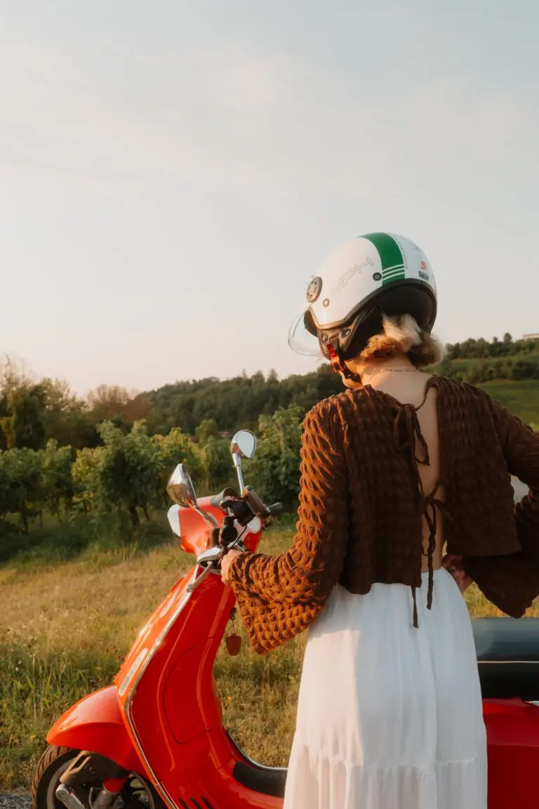 vrouw met helm op een rode Vespa in een wijngaard in Veneto bij zonsondergang