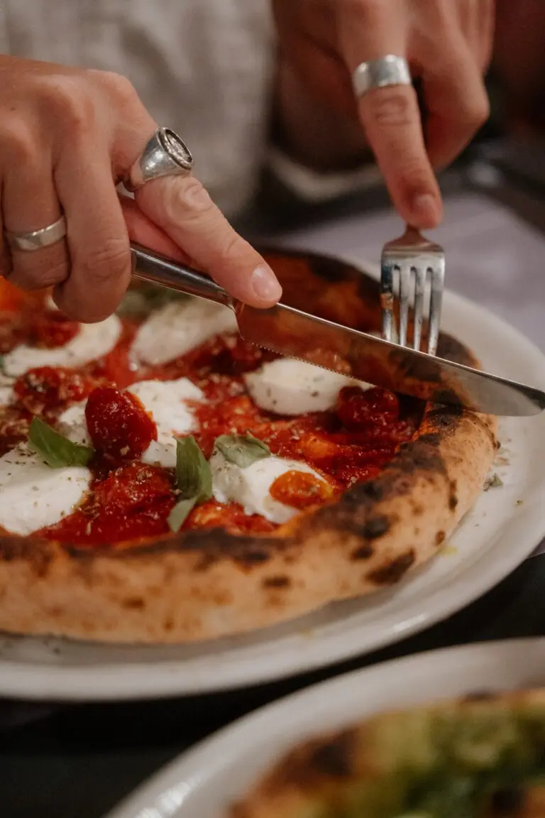 handen die een verse pizza met mozzarella en basilicum aansnijden