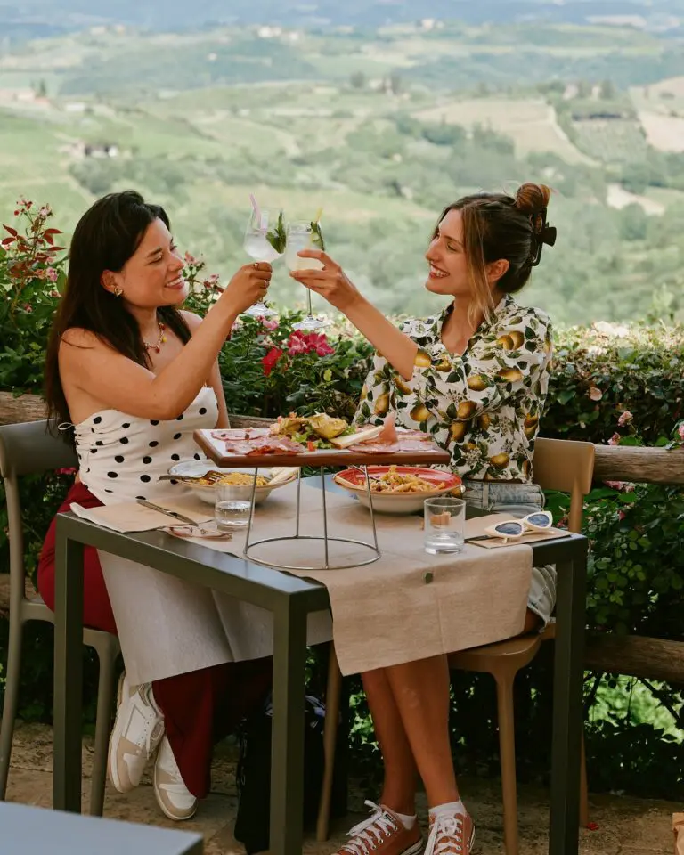 two women toasting drinks at an outdoor restaurant in Tuscany