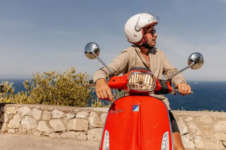 man on red Vespa scooter overlooking the sea