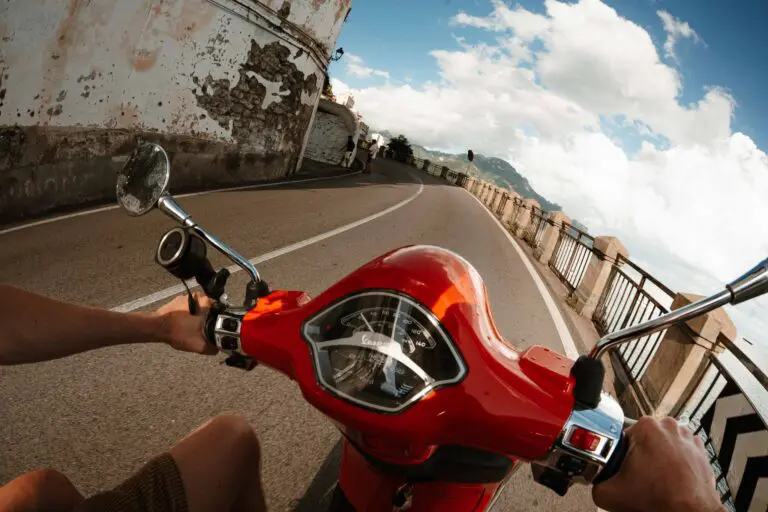 person riding a red Vespa scooter on a coastal road in Amalfi