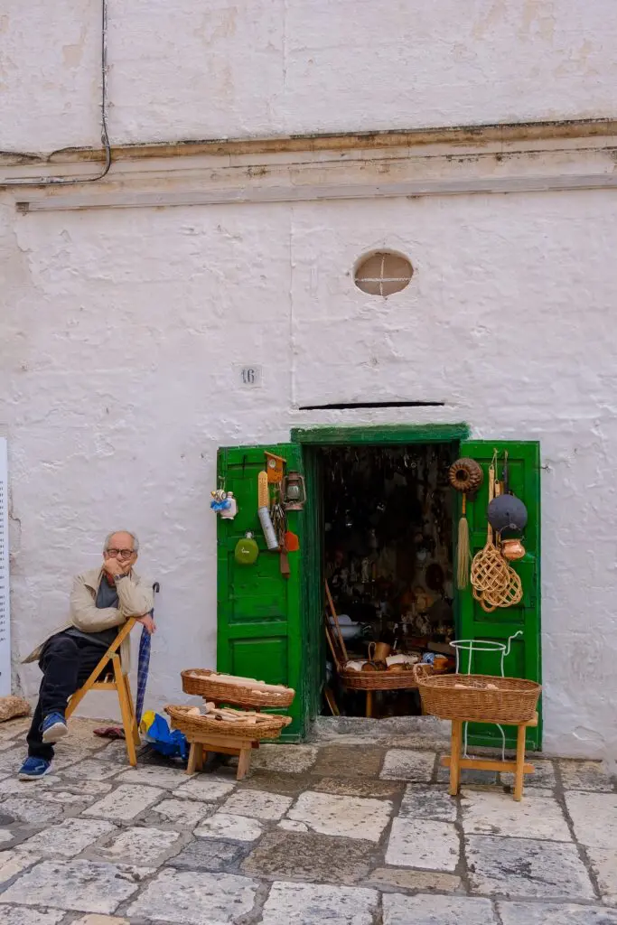man sitting outside a shop with green doors in Ostuni, Puglia