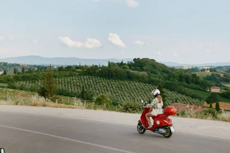 woman riding red vespa through tuscan countryside