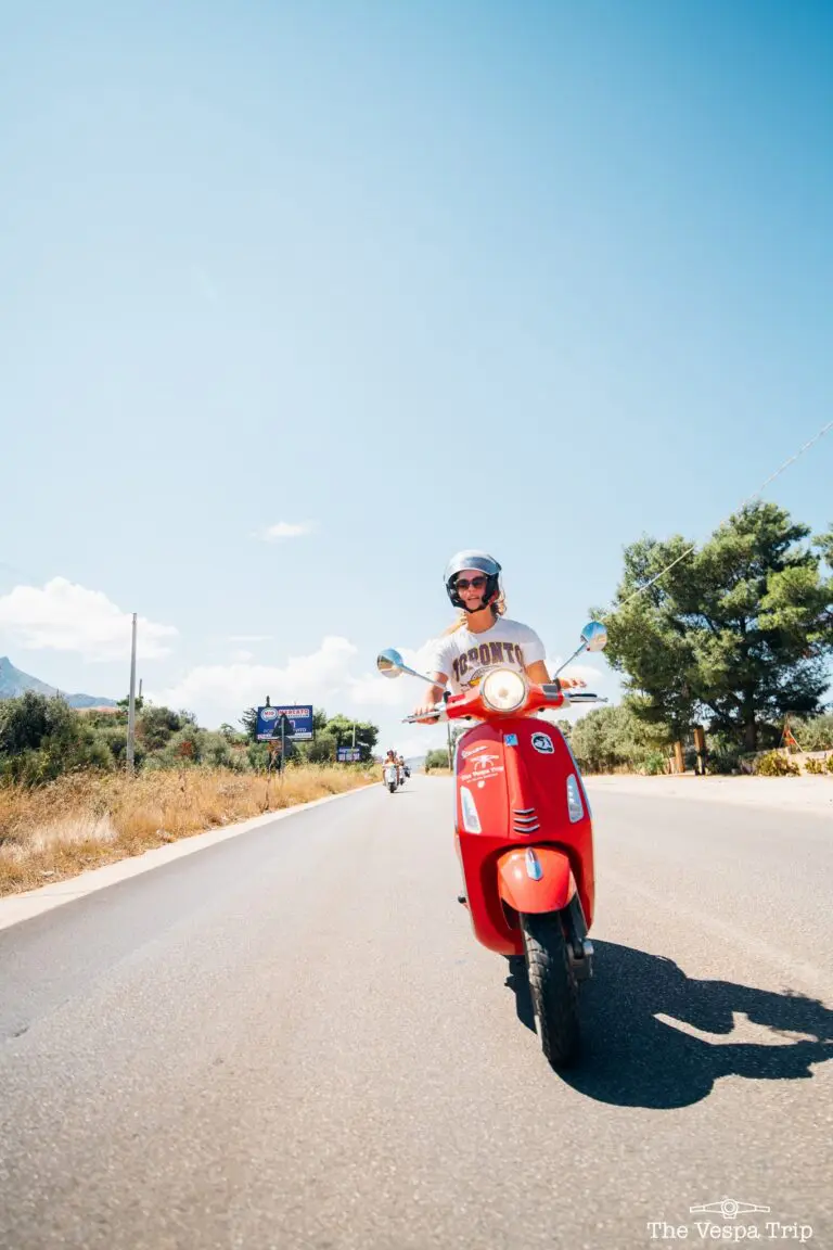 person riding a red Vespa scooter on a sunny road in Sicily