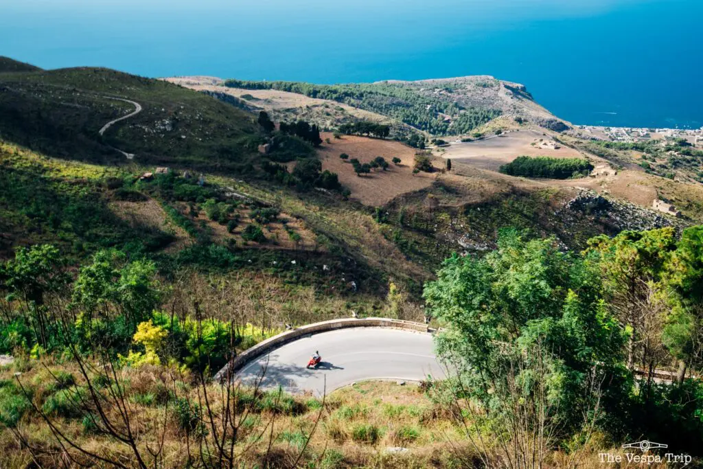 red vespa on winding road overlooking the sea in Sicily
