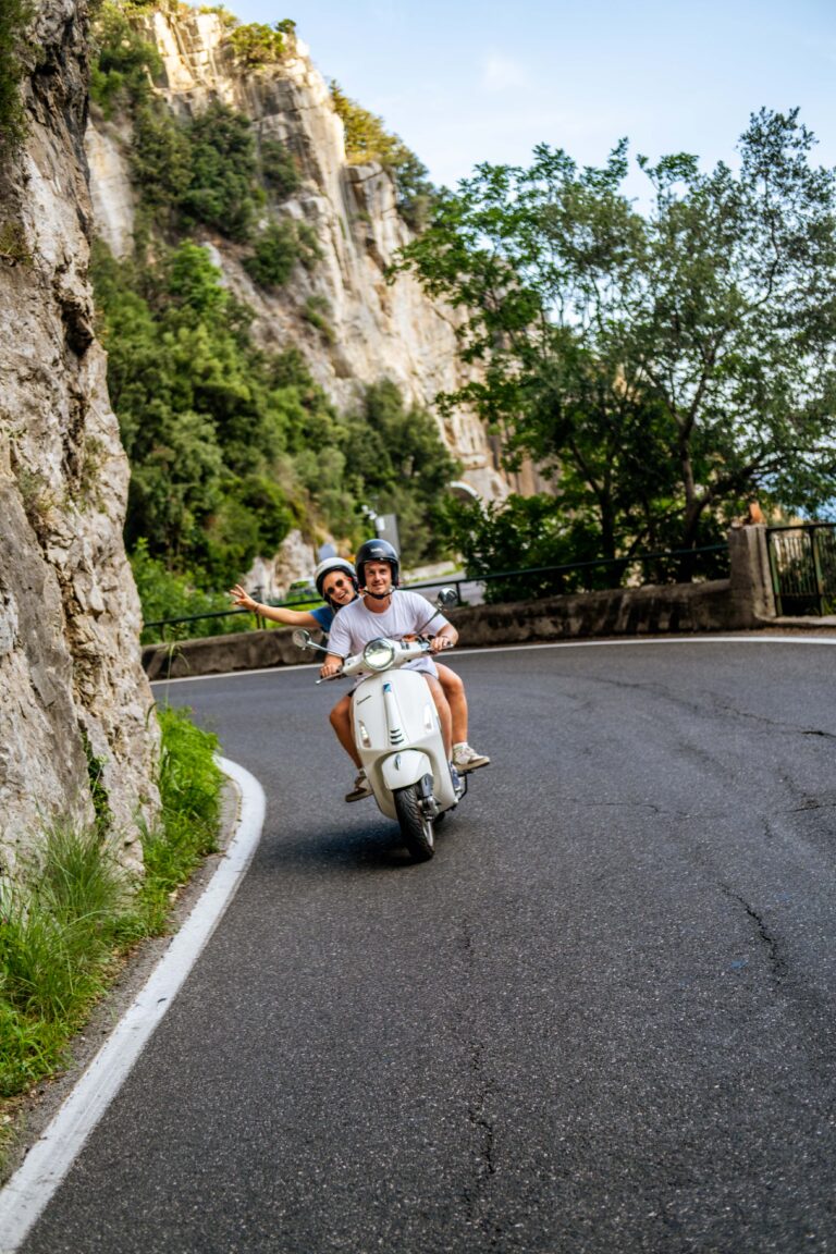 Two people riding a white Vespa along the Amalfi coast