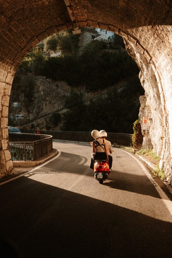 koppel op een rode scooter dat door een boog in Amalfi rijdt