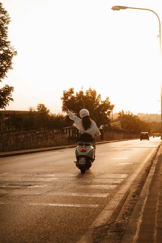 woman on a scooter with arm raised at sunset in Amalfi