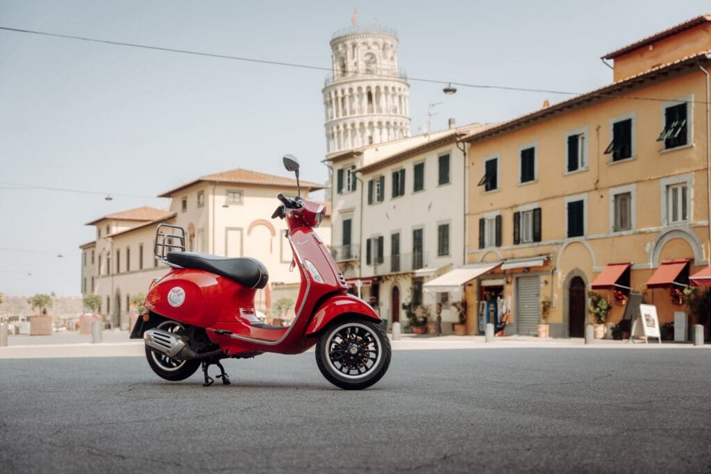 red Vespa-scooter geparkeerd op een piazza met de scheve toren van Pisa