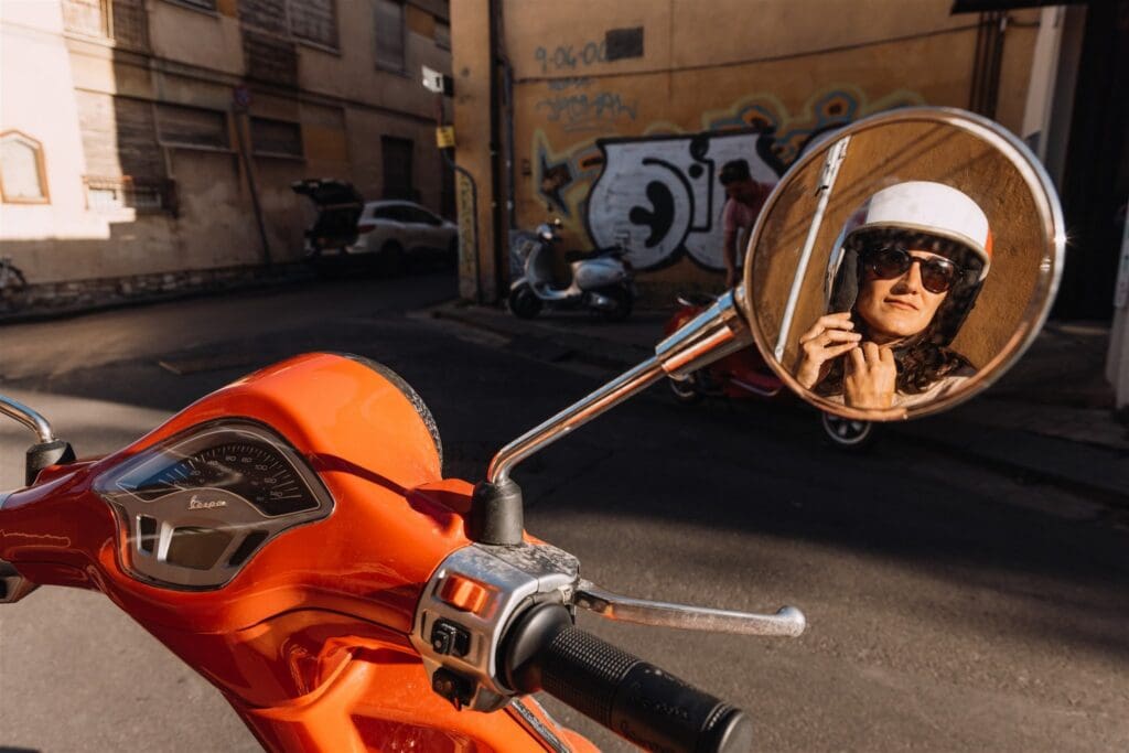 vrouw met helm weerspiegeld in de scooterachteruitkijkspiegel in Toscane