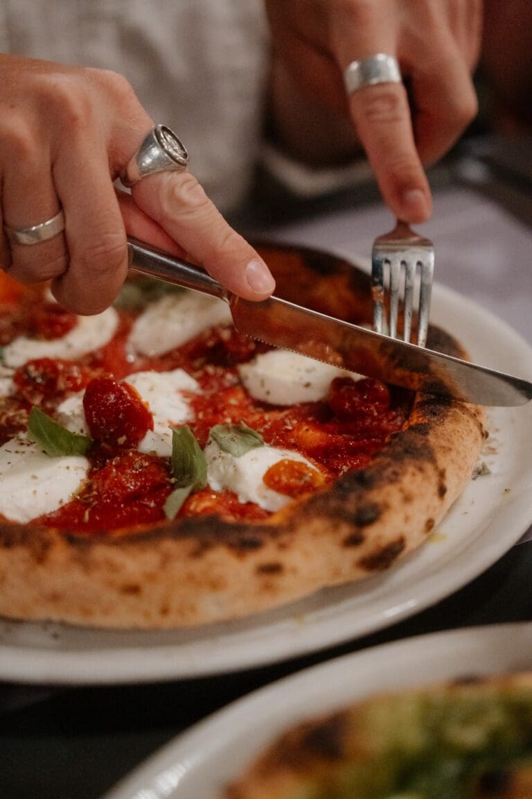 hands cutting a fresh pizza with mozzarella and basil