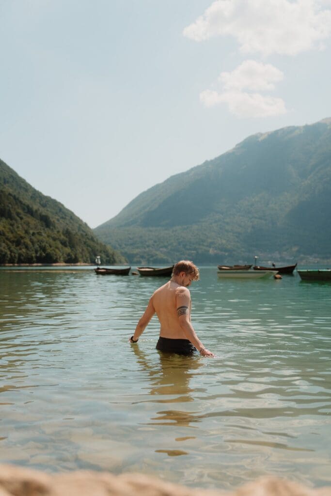 man wading in a lake with mountains and boats