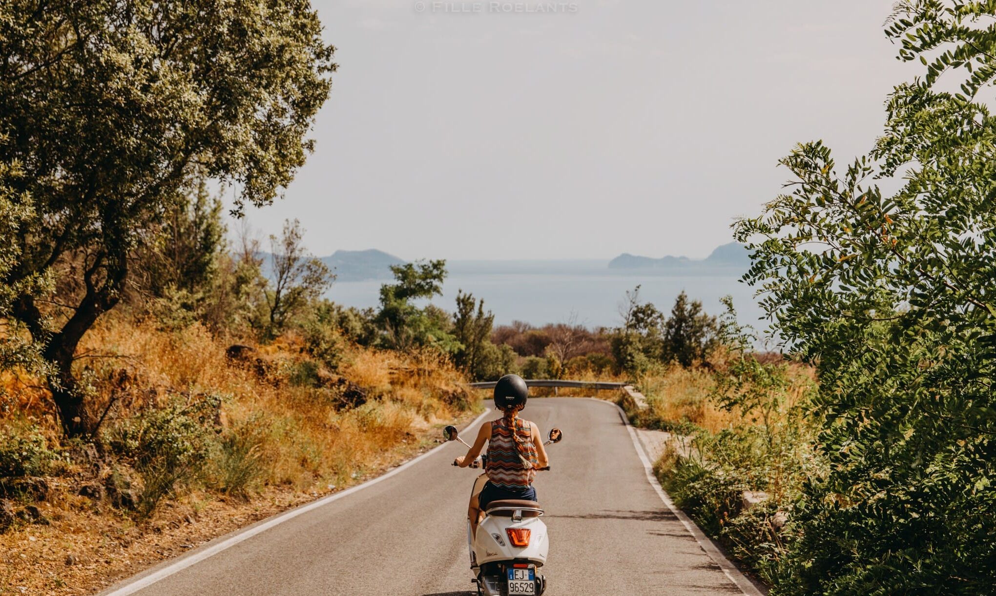 person riding a white Vespa on a coastal road